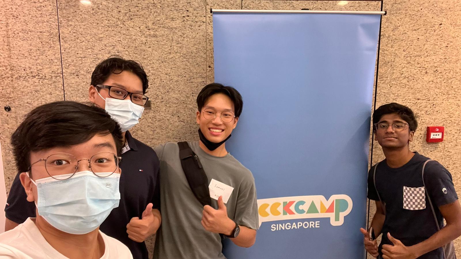 Four people smiling in front of a vertical banner with the words 'Geekcamp Singapore' on it